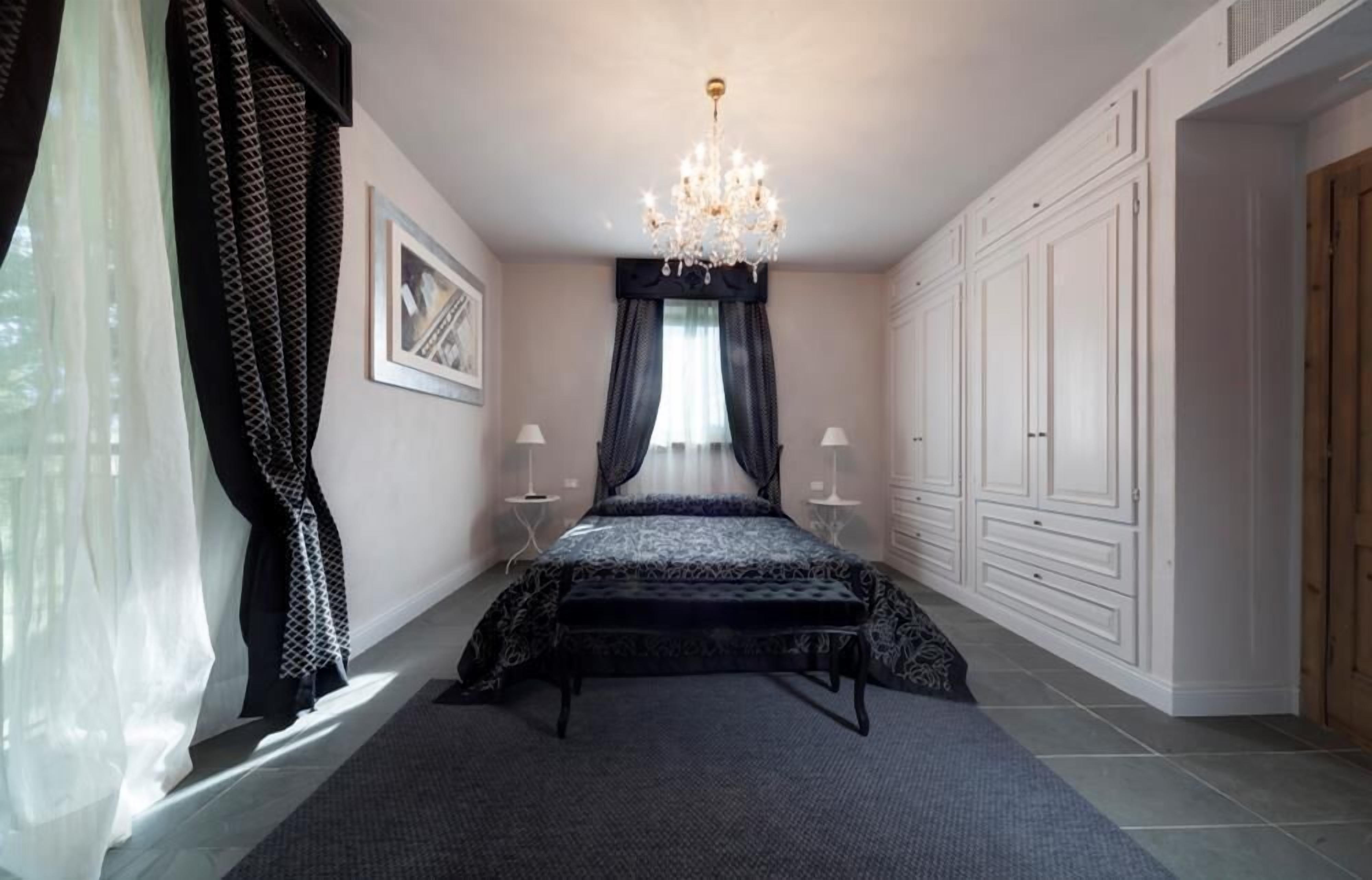 Een slaapkamer met een bed, een kroonluchter, een kledingkast en een raam met gordijnen.