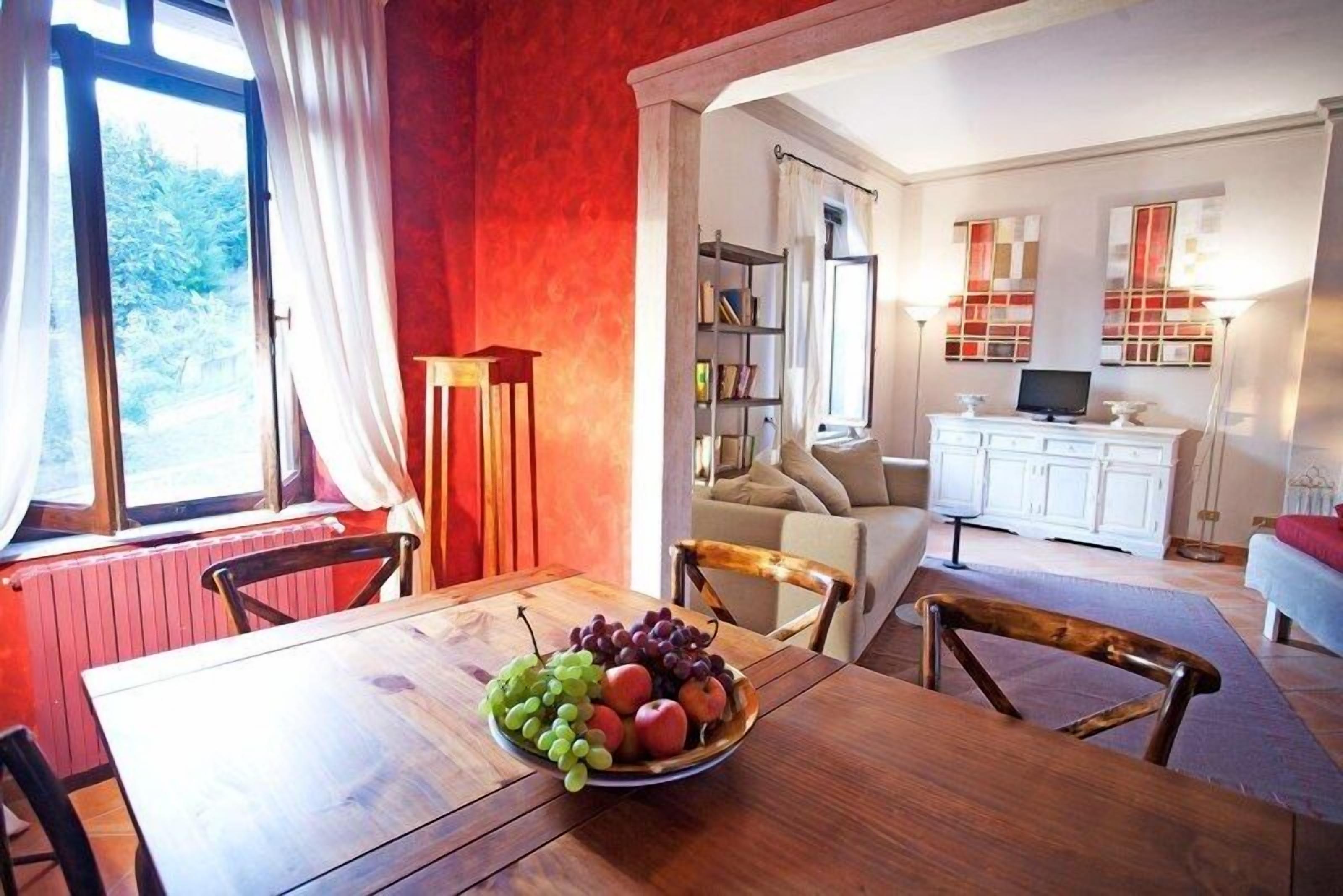 Un coin repas avec une table et des chaises en bois, un saladier rempli de fruits, et une vue sur la cuisine et le salon.
