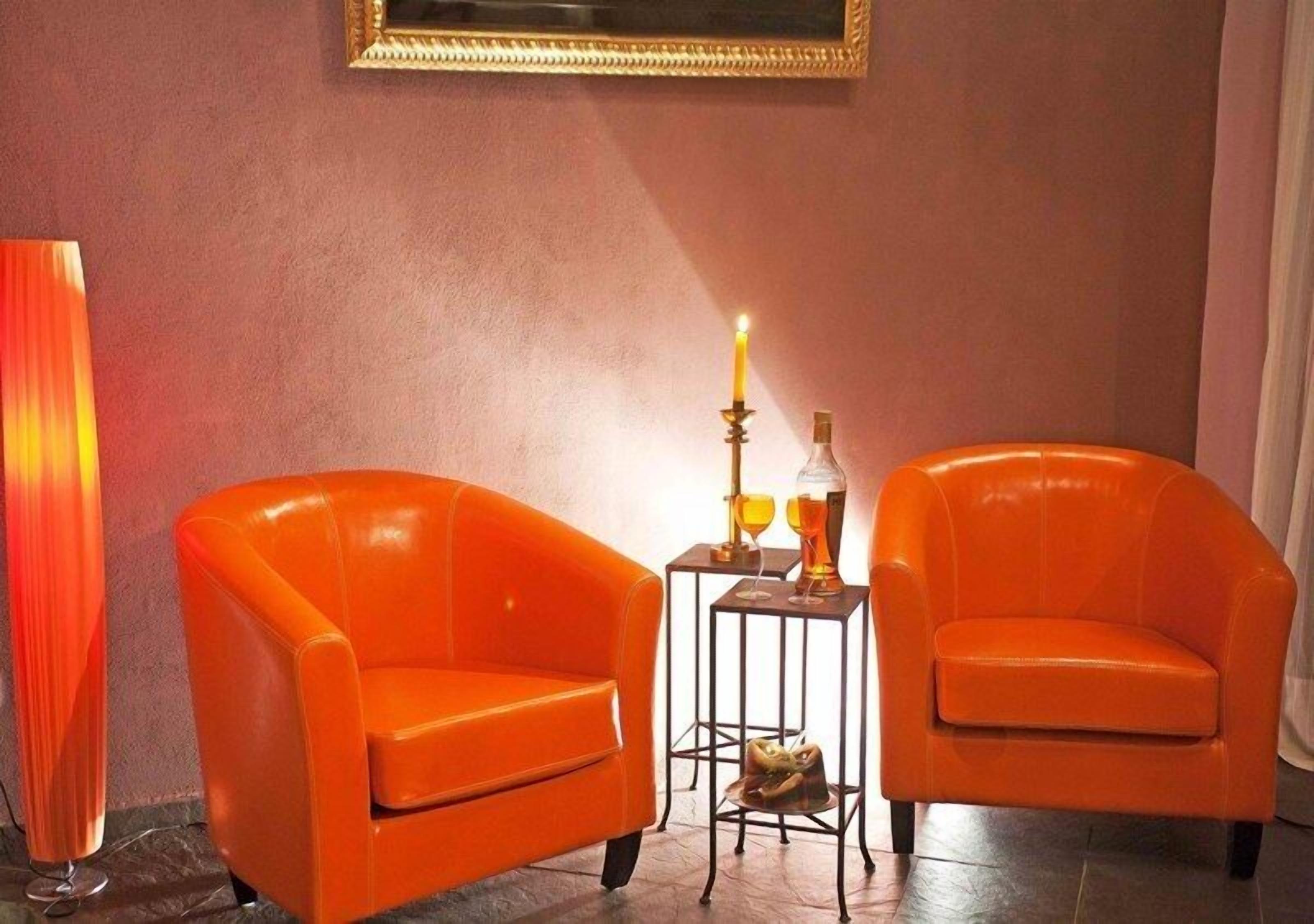 Two orange armchairs, a tall floor lamp, and a small table with a candle and a bottle.