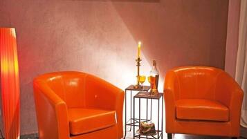 Two orange armchairs, a tall floor lamp, and a small table with a candle and a bottle.