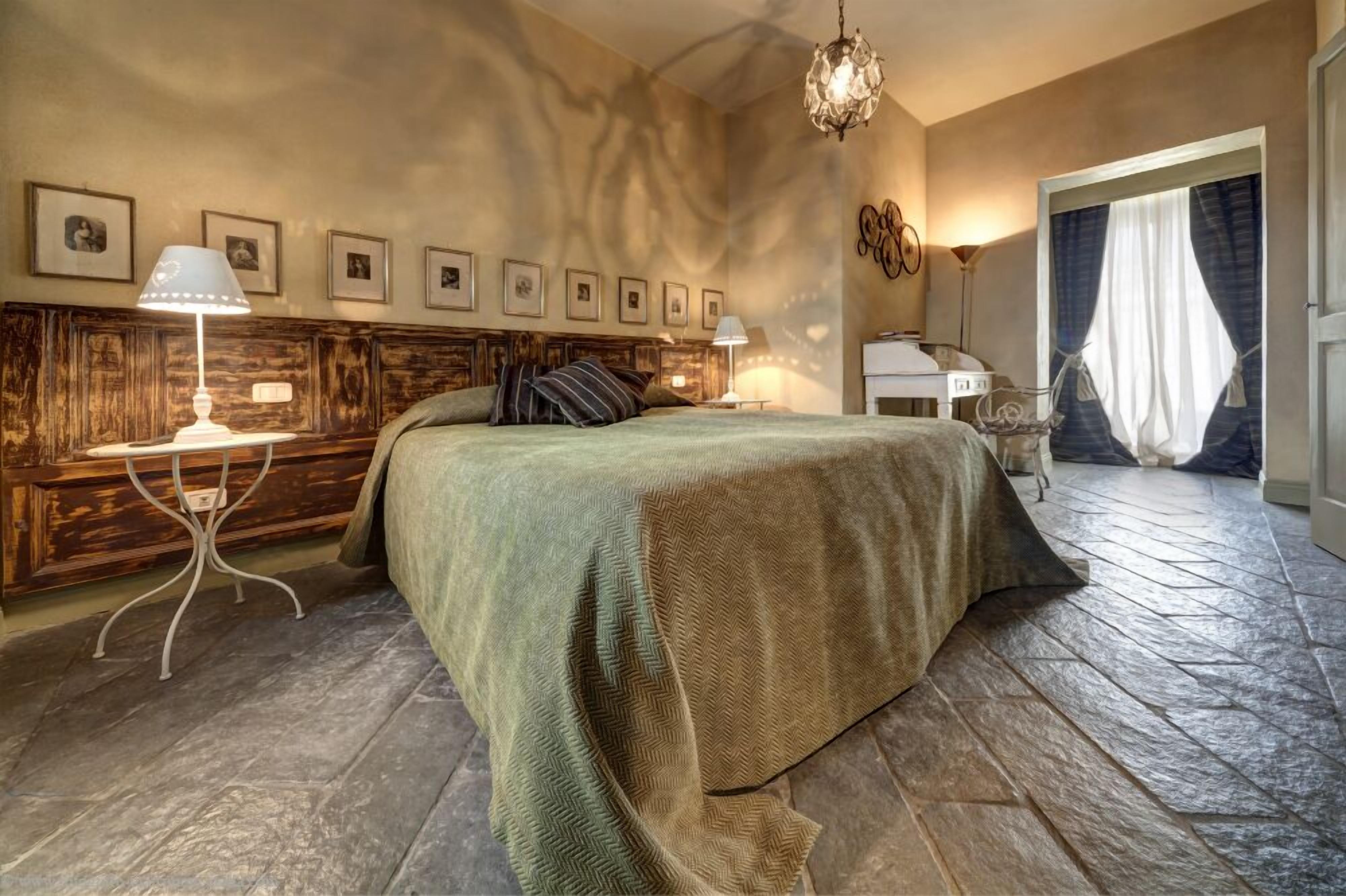 Un dormitorio con una cama grande, paneles de madera en las paredes, cuadros enmarcados, un escritorio con una silla y una araña.