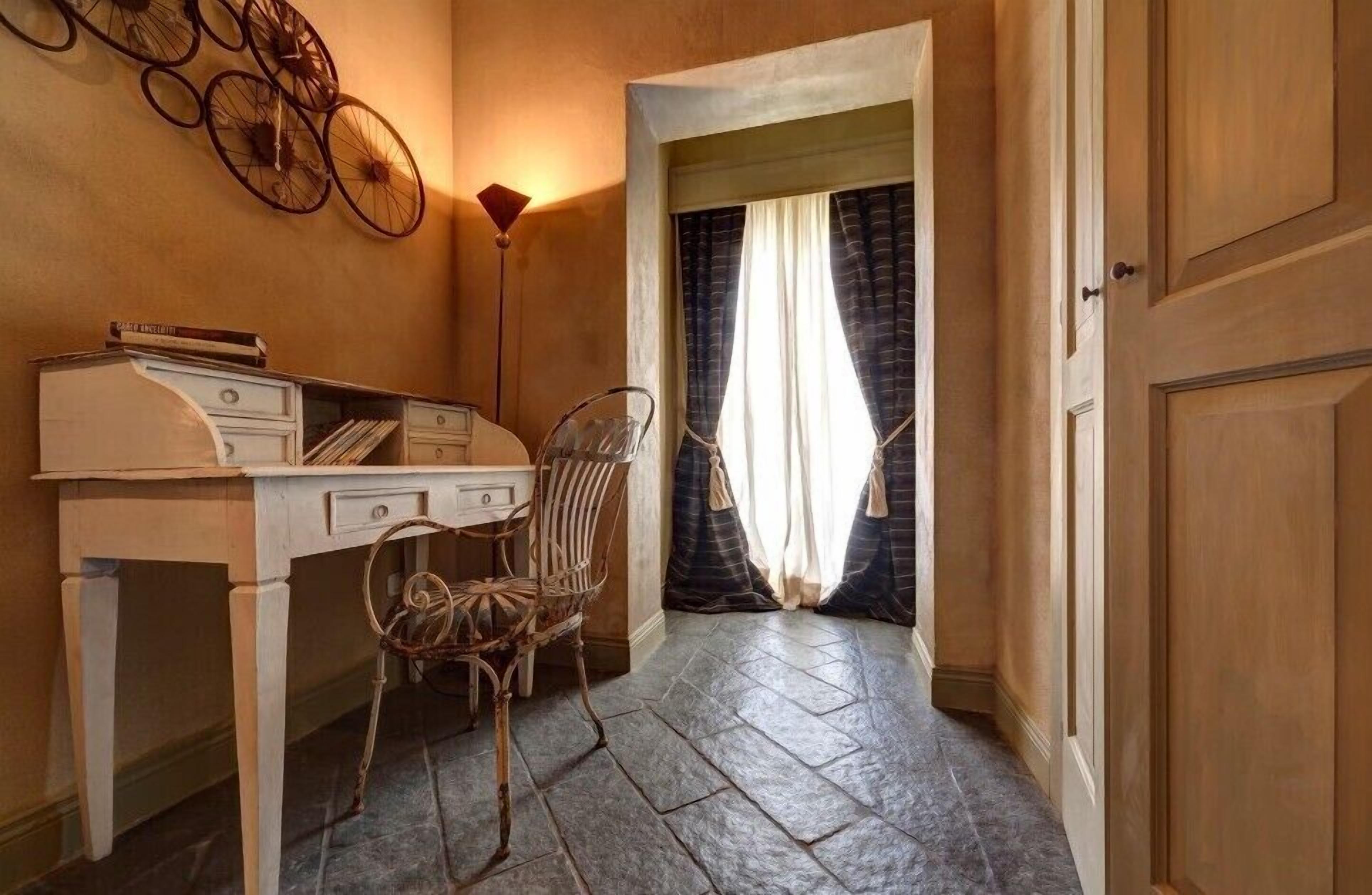 A narrow hallway with a desk and chair, a bicycle, and a door with curtains.
