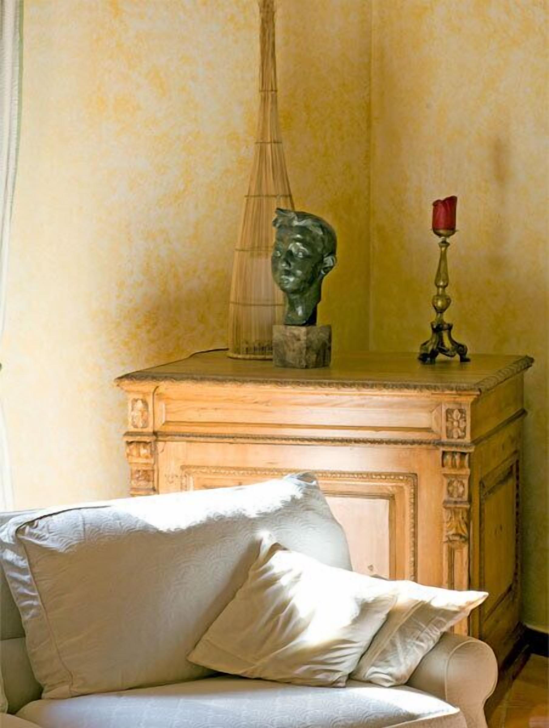 Um quarto com sofá bege, mesa lateral de madeira com uma escultura e uma rosa vermelha, e um vaso de vidro transparente.