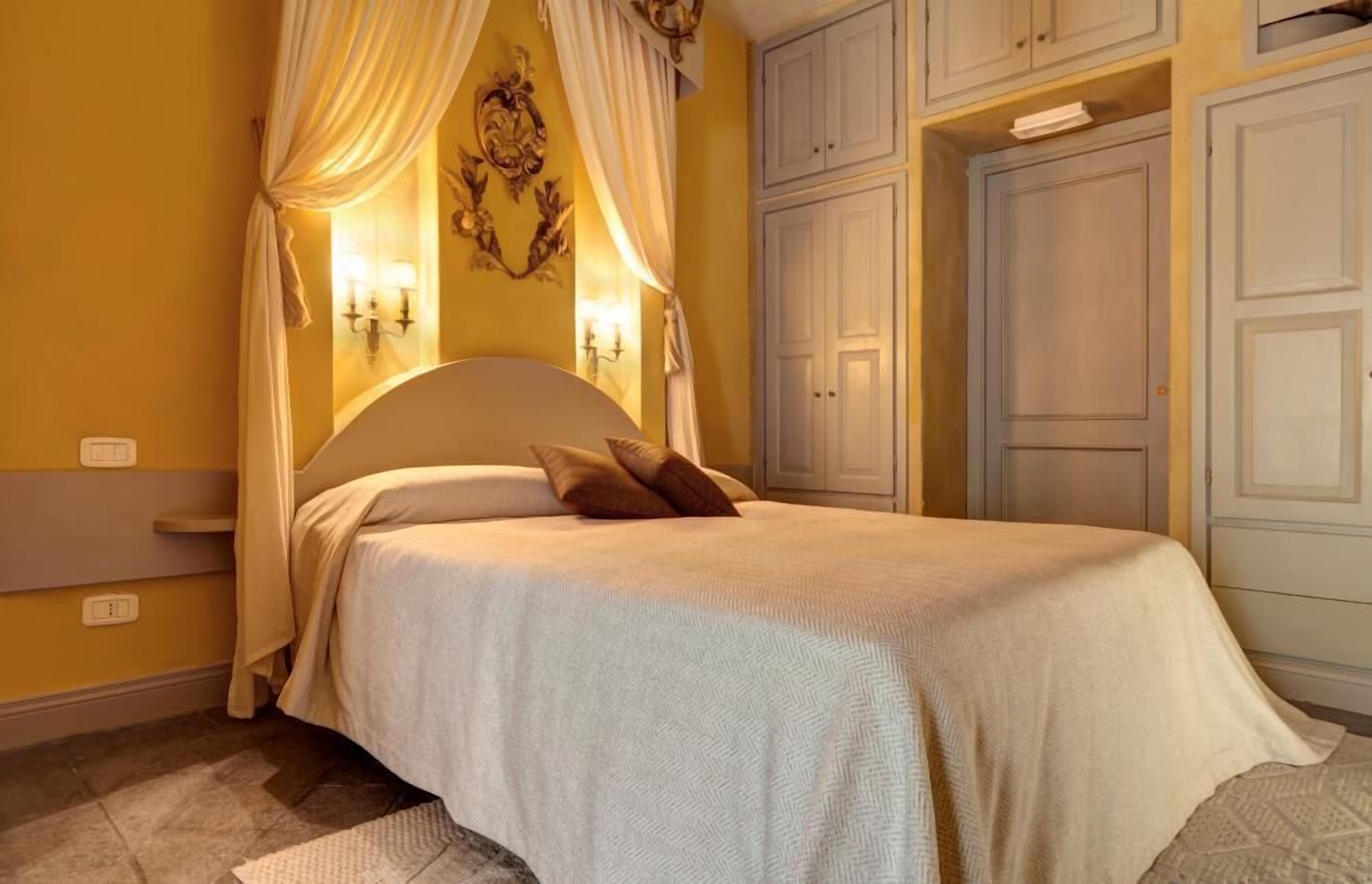 A bedroom with a bed, curtains, wall sconces, and built-in cabinets.