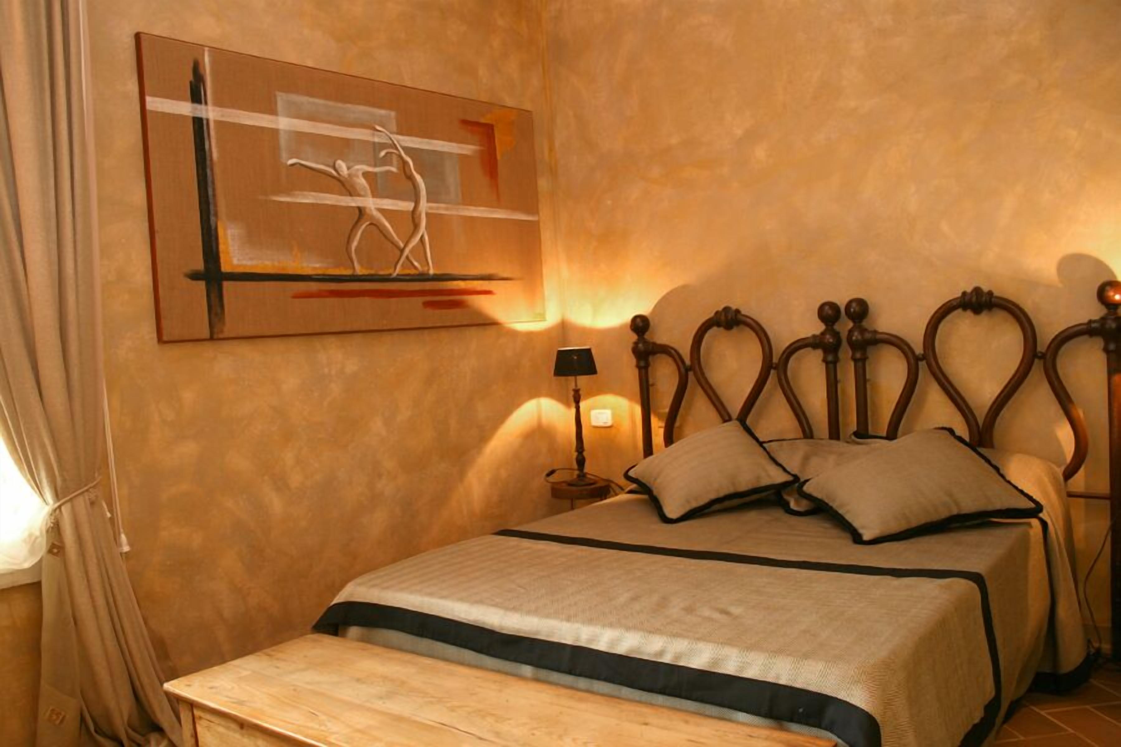 Een slaapkamer met een bed, nachtkastje, lamp en een schilderij aan de muur.