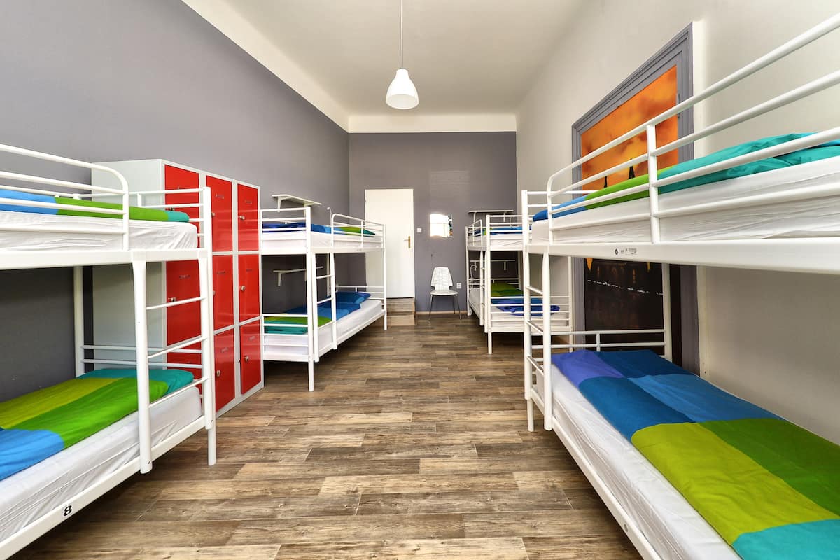 A dormitory room with bunk beds, wooden flooring, and a white pendant light.