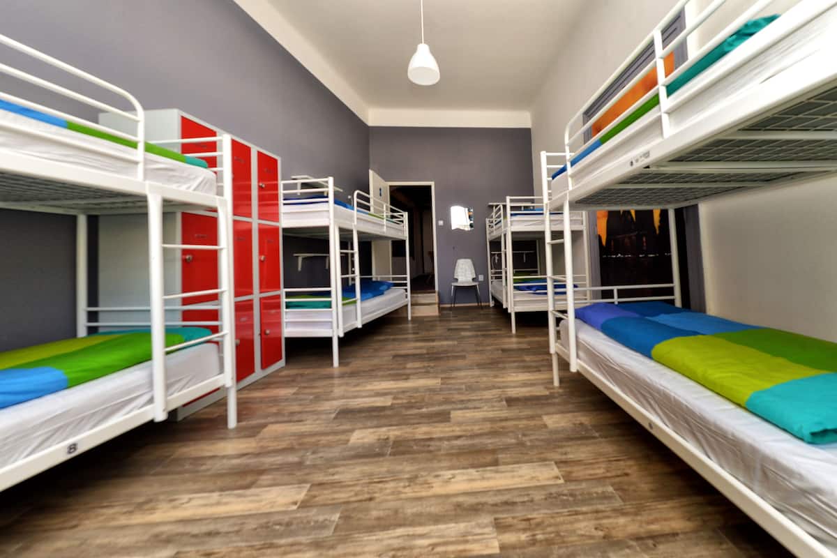A dormitory room with bunk beds, wooden flooring, and a white pendant light.