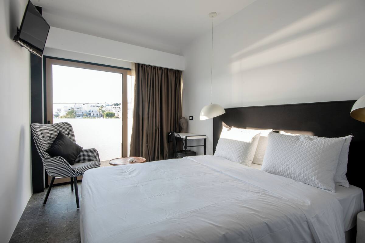A hotel room with a large bed, a desk, a chair, and a TV mounted on the wall.