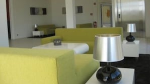A modern hotel room with a yellow sofa, a white armchair, a small table with a lamp, and a bed in the background. - Qualitel Hotel Hilpoltstein (Hilpoltstein)
