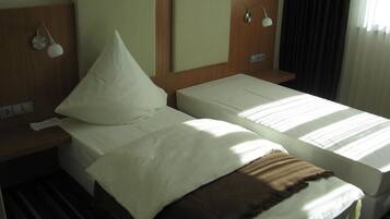Een hotelkamer met twee eenpersoonsbedden, een houten hoofdbord, nachtlampjes en een raam met gordijnen.
