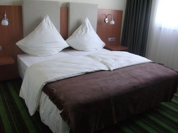 A hotel room with a bed, two nightstands, a brown throw blanket, and a window with curtains.