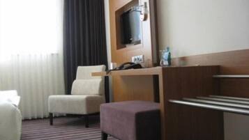 A hotel room with a bed, a desk with a chair, a television, and a window with curtains.