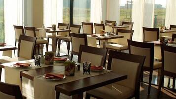 Un restaurante con varias mesas y sillas, ventanas amplias y vistas al exterior.
