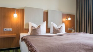 A hotel room with a bed, two bedside tables, a nightstand with a lamp, and a mirror on the wall. - Qualitel Hotel Hilpoltstein (Hilpoltstein)
