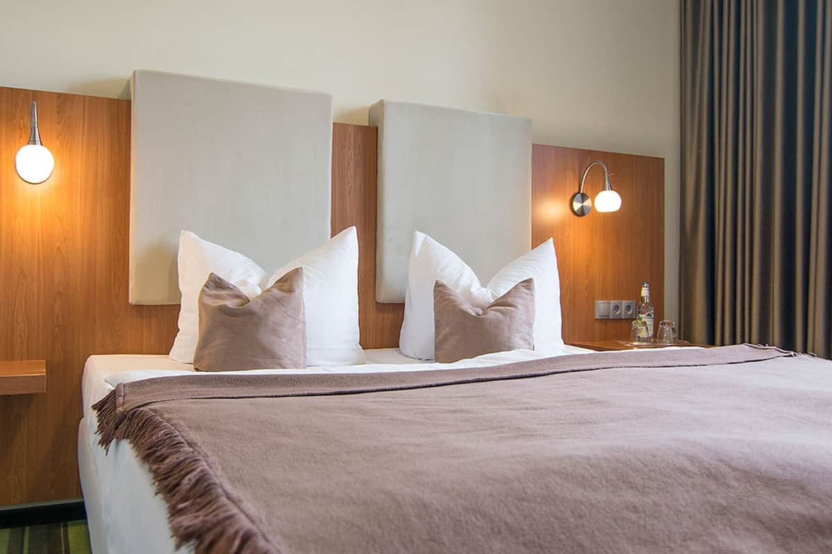 Una habitación de hotel con una cama, dos mesitas de noche, una mesita con lámpara y un espejo en la pared.