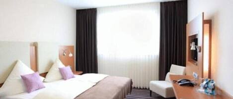 A hotel room with a bed, a desk, a chair, and a large window with curtains.