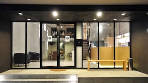 A modern interior with a reception desk, seating area, and a staircase leading to an upper level. - Luz Hostel (Bangkok)