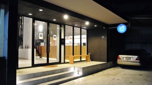 A modern building with a reception desk, a bench outside, and a car parked nearby. - Luz Hostel (Bangkok)