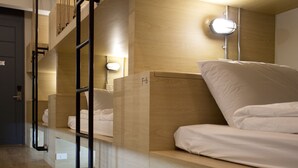 A hotel room with bunk beds, a bedside lamp, and a wooden headboard. - Luz Hostel (Bangkok)