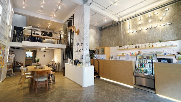 A modern interior with a wooden reception desk, a glass display case, and a staircase leading to an upper level. - Luz Hostel (Bangkok)