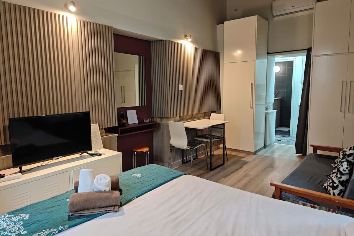 Habitación de hotel con cama, escritorio, televisión y baño visible a través de una puerta abierta.