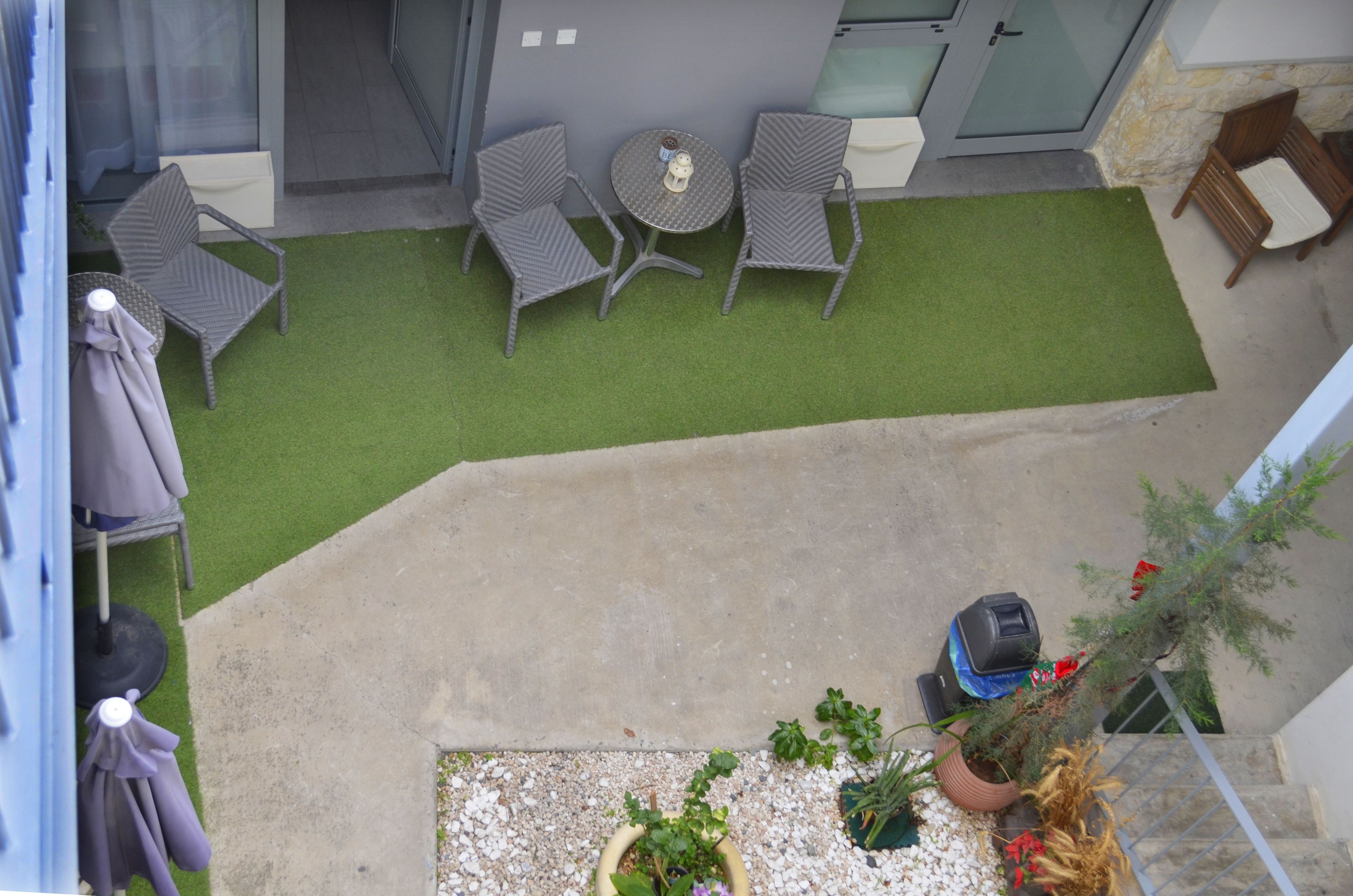 A rooftop patio with artificial grass, two wicker chairs, a small round table, and potted plants.