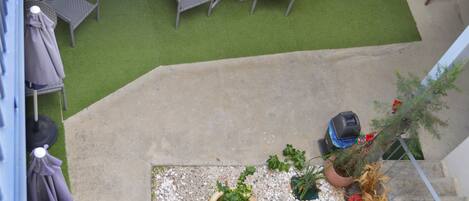 Une terrasse sur le toit, avec un revêtement d’herbe artificielle, deux fauteuils en osier, une petite table ronde et des plantes en pot.