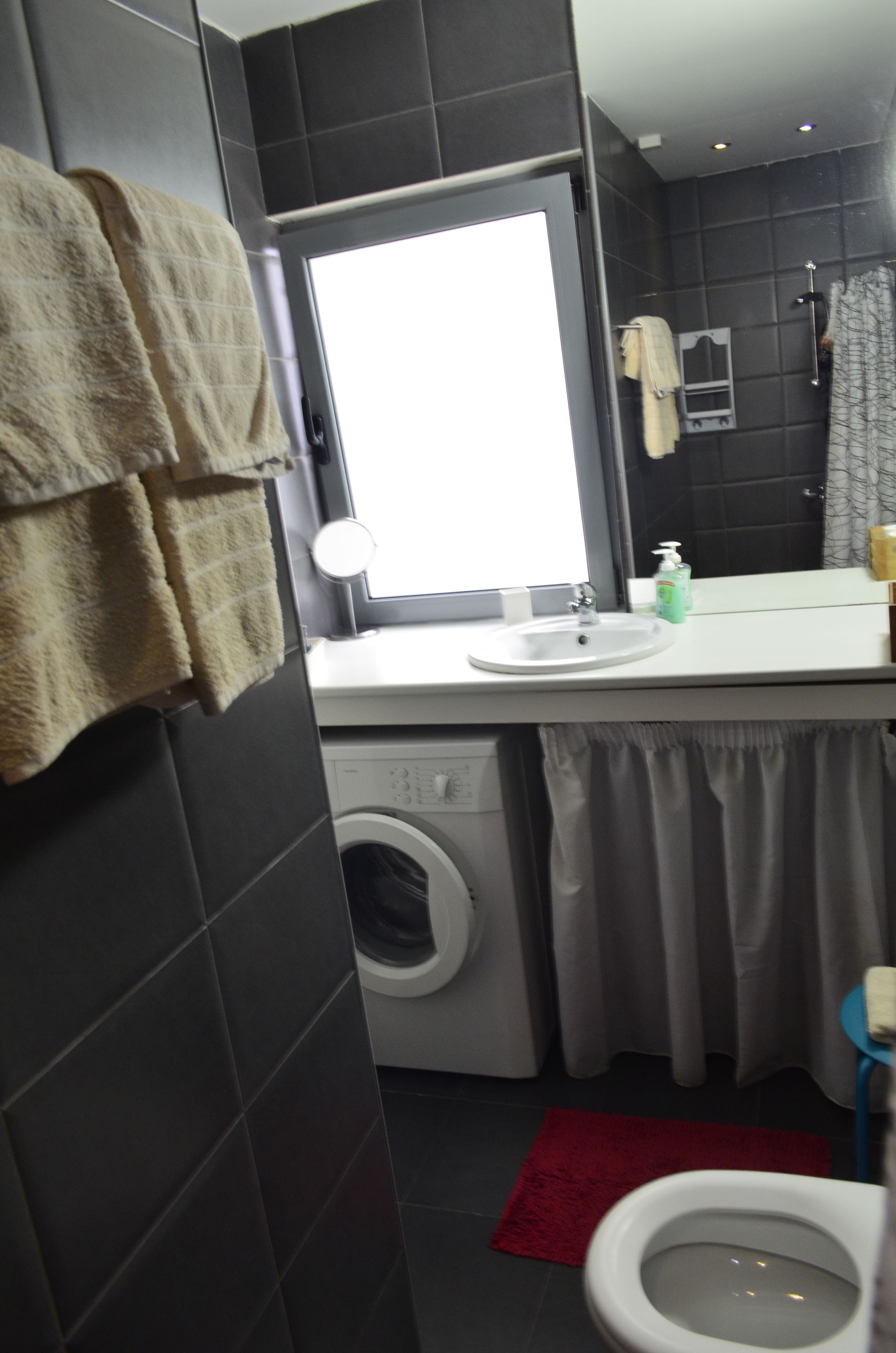 Un baño con lavadora, lavamanos, espejo e inodoro.