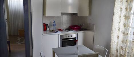 Una cocina compacta con alacenas blancas, horno de acero inoxidable y un rincón comedor con dos sillas.