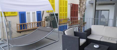 Ein Balkon mit Gartenmöbeln, darunter eine Sitzecke mit Sofa und einem Tisch, sowie einer Hängematte.
