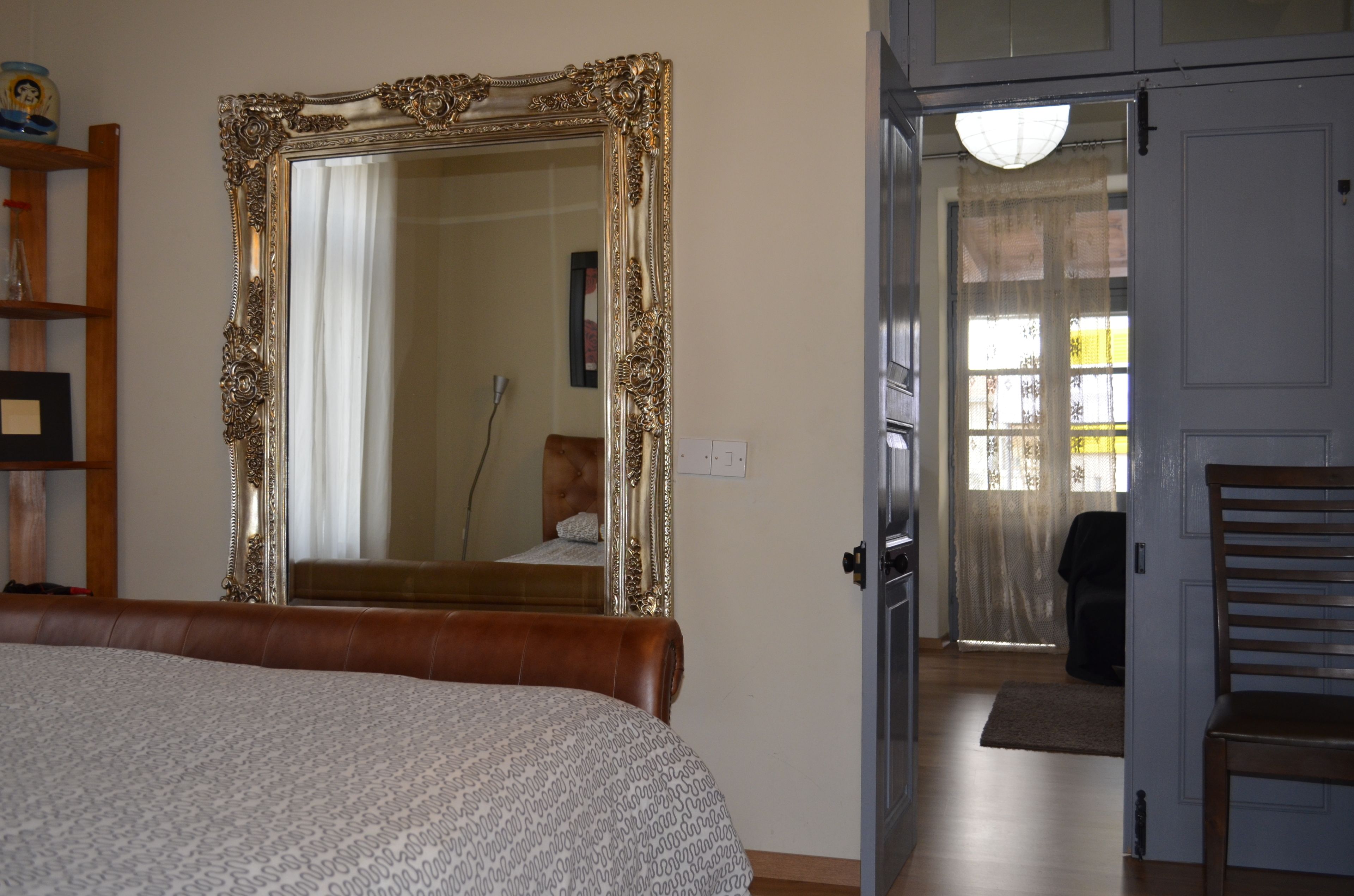 A bedroom with a large ornate mirror, a bed with a patterned bedspread, and a wooden chair.