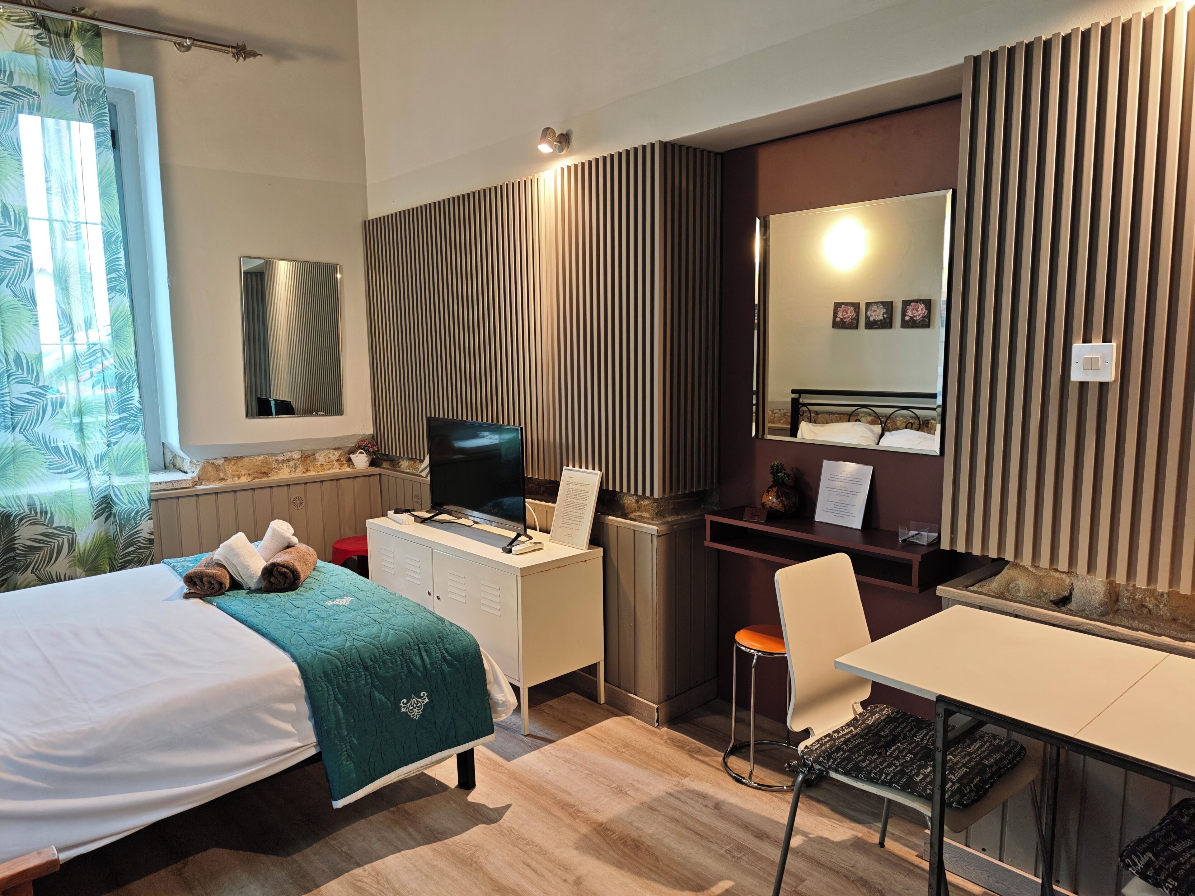 A hotel room with a bed, desk, chair, TV, and a mirror.