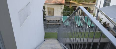 Escadaria que dá para uma varanda com mesa e cadeiras, cercada por uma parede branca e um edifício com telhado de azulejos.