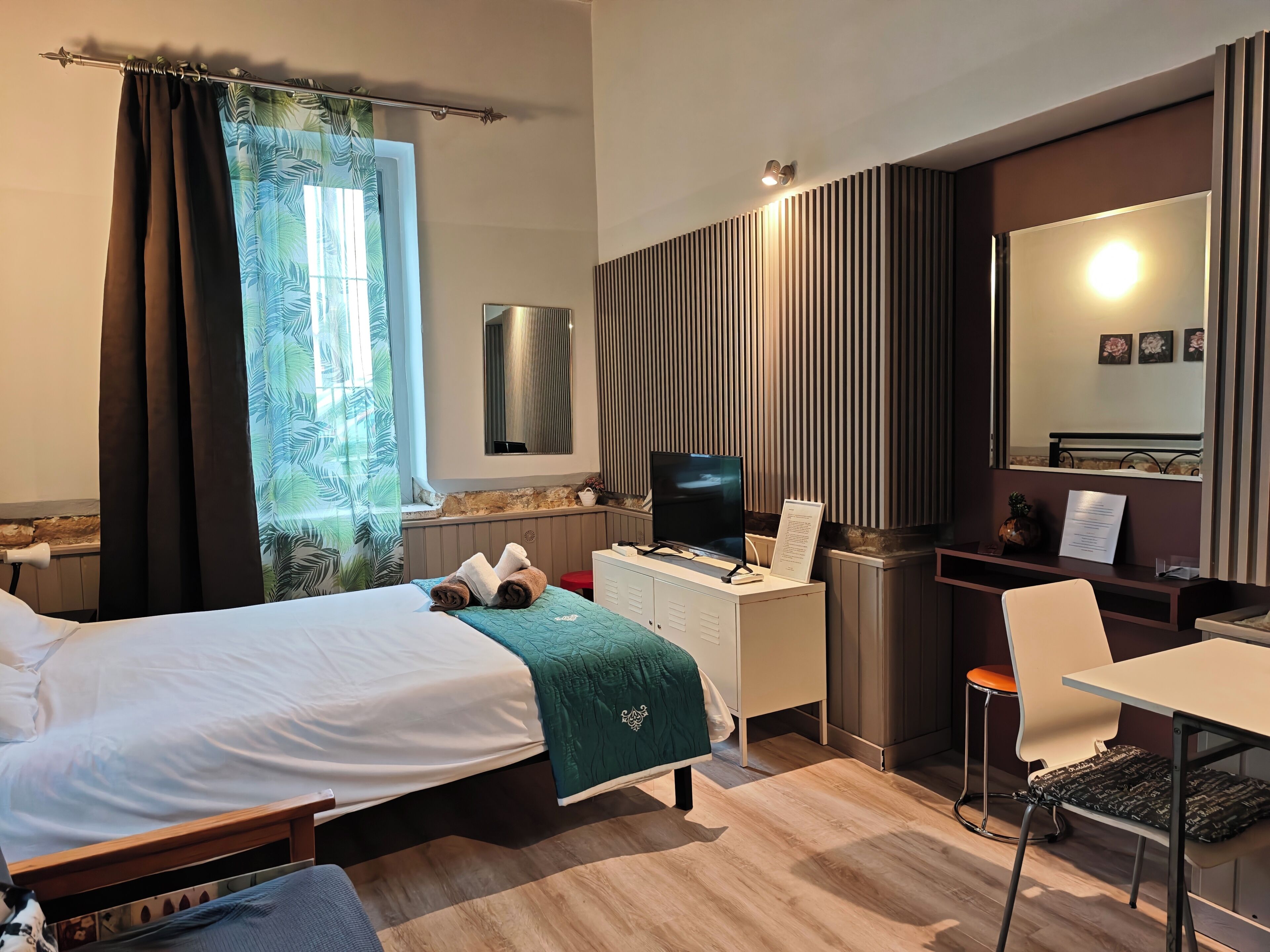 A hotel room with a bed, a desk, a chair, a TV, and a mirror.