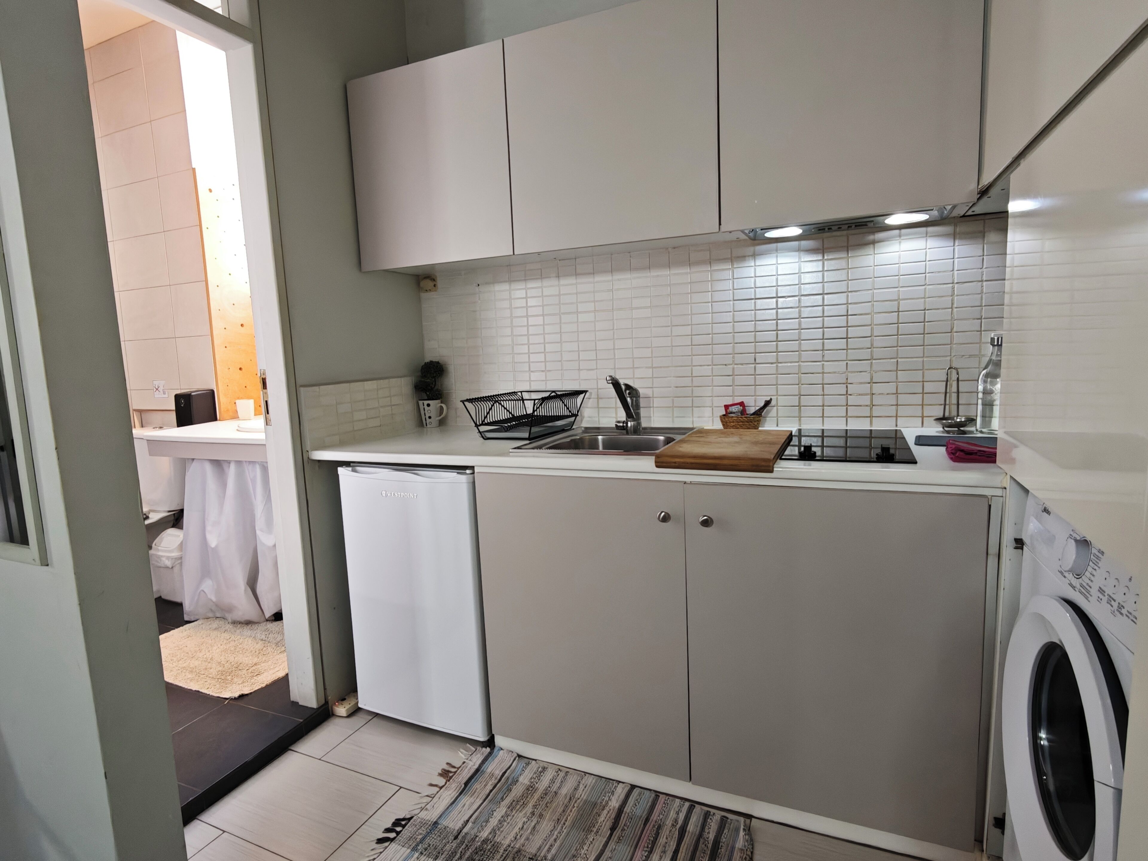 A compact kitchen with white cabinets, a dishwasher, a washing machine, and a tiled backsplash.