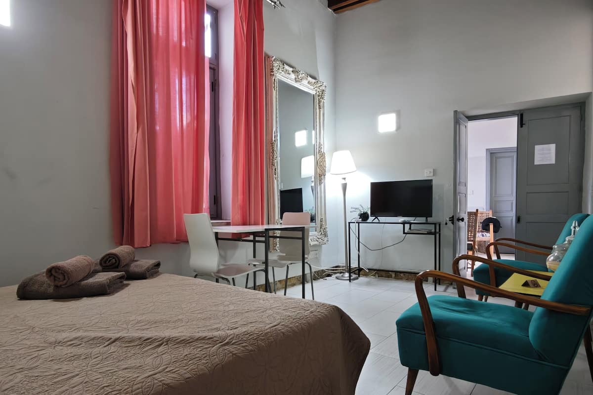 Habitación de hotel con cama, escritorio, silla, televisor, espejo y sillón color verde azulado.