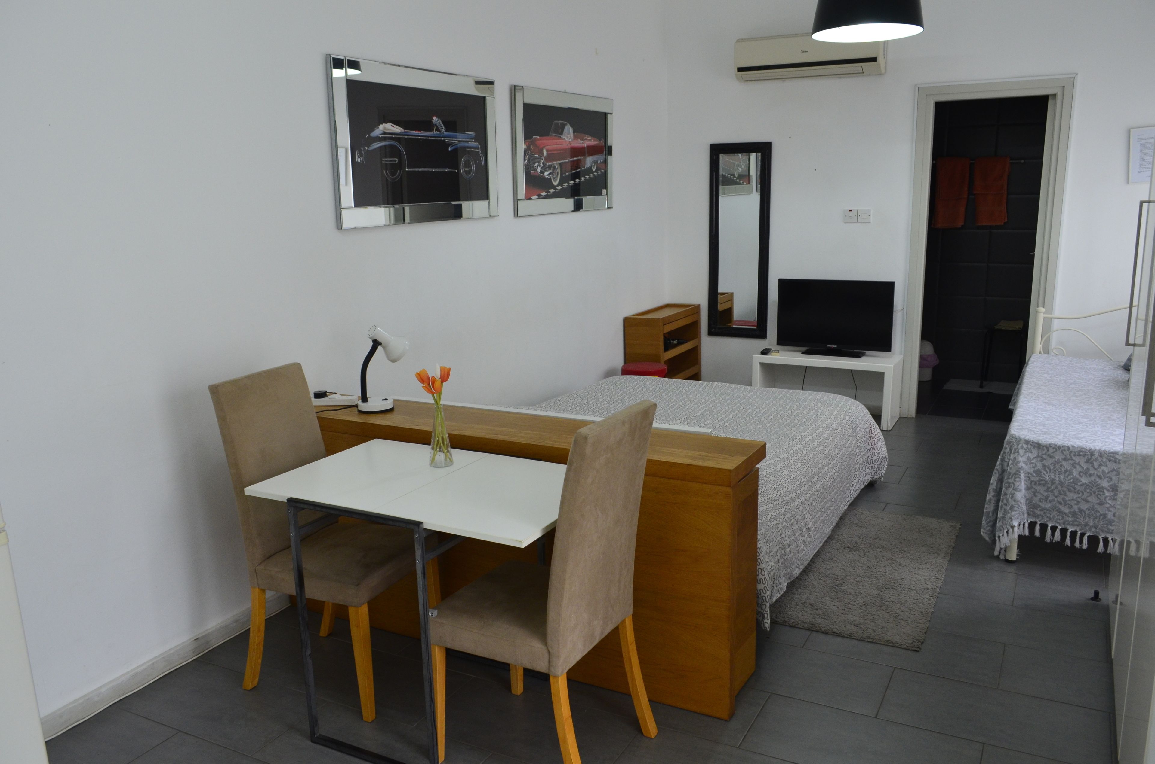 Una habitación de hotel con cama, escritorio, silla, televisor y espejo.