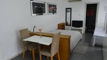 Una habitación de hotel con cama, escritorio, silla, televisor y espejo.