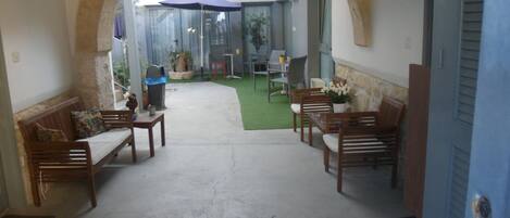 An indoor patio area with a concrete floor, wooden benches, and a glass door leading to an outdoor space.