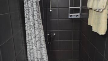Een kleine, donkere badkamer met een wit toilet, een douche met een decoratieve gordijn en een handdoekrek met een handdoek.