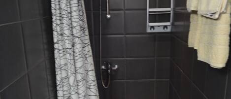 Un baño pequeño y oscuro, con inodoro blanco, ducha con cortina estampada y toallero con una toalla.