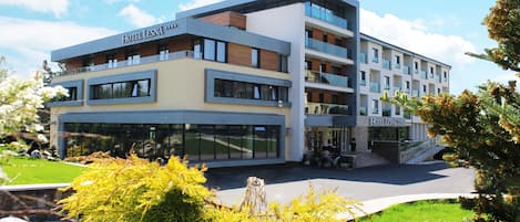 A multi-story hotel with a modern design, featuring balconies, large windows, and a landscaped garden area.