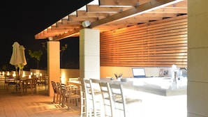 An outdoor bar area with wooden beams, a counter, and bar stools. - Niovi Apartments (Kassandra)