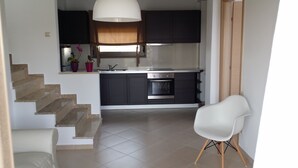 A modern kitchen with dark cabinets, a built-in oven, and a white chair. - Niovi Apartments (Kassandra)