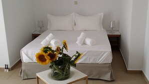 A neatly made bed with white linens, two rolled towels, and a vase with sunflowers on a bedside table. - Niovi Apartments (Kassandra)