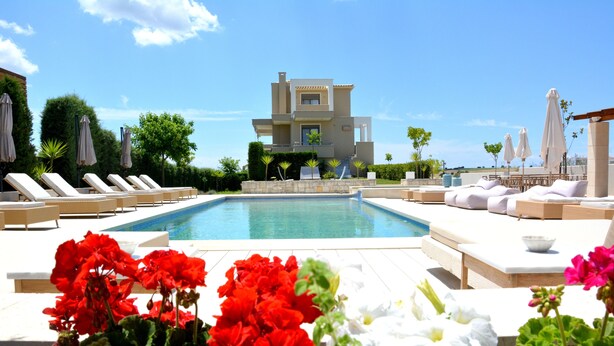 A pool area with lounge chairs and a modern building in the background. - Niovi Apartments (Kassandra)