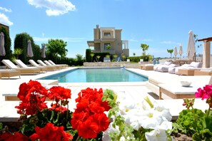 A pool area with lounge chairs and a modern building in the background. - Niovi Apartments (Kassandra)