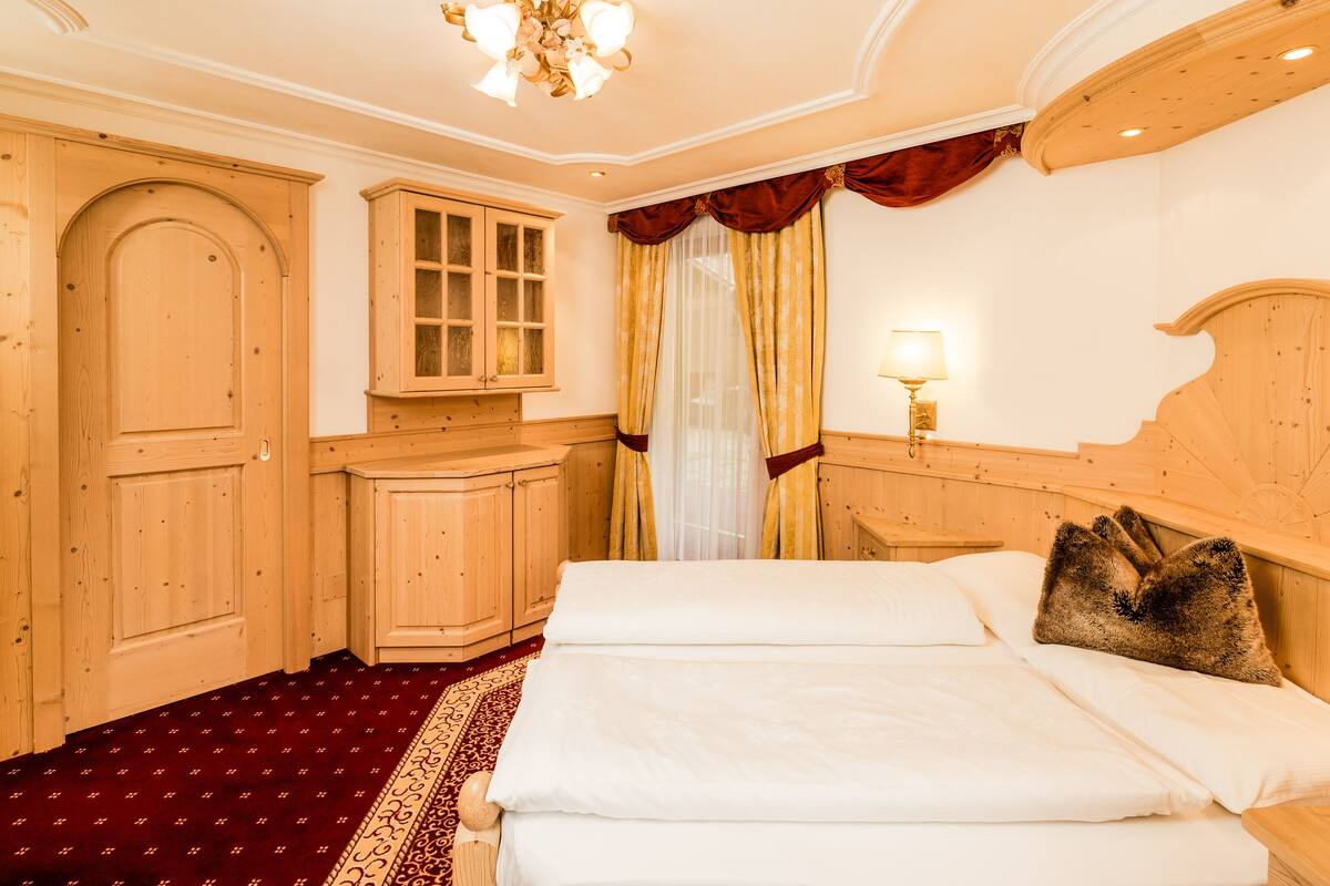 A hotel room with a large bed, wooden wardrobe, and a chandelier.
