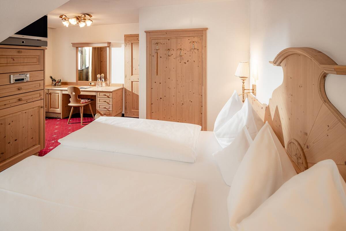 A bedroom with a large bed, wooden wardrobe, and a desk with a chair.