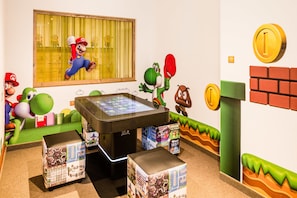 Un espace de jeux pour enfants décoré avec des autocollants muraux à l’effigie de Mario et Luigi, une console Nintendo DS et une console de jeux sur le thème de Mario.
